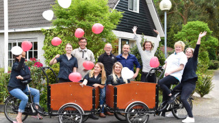 Grupo celebrando con globos y bicicletas frente a Bungalowpark Het Verscholen Dorp, Gelderland, Países Bajos.