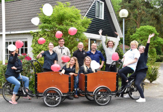 Grupo celebrando con globos y bicicletas frente a Bungalowpark Het Verscholen Dorp, Gelderland, Países Bajos.