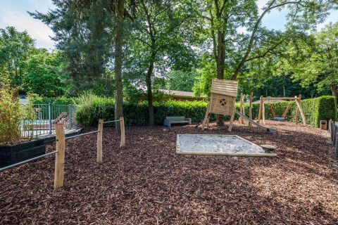 Speeltuin met zandbak, houten speelhuis, schommels en glijbaan in Bungalowpark Het Verscholen Dorp, Gelderland.
