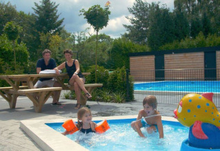 Famiglia al tavolo da picnic, bambini che giocano in piscina con fontana presso Het Verscholen Dorp.