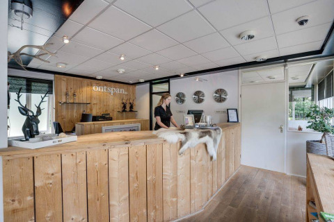 Receptionen på Bungalowpark Het Verscholen Dorp i Gelderland, Holland, med træinteriør og en receptionist.