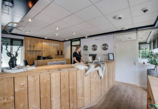 Rezeption im Bungalowpark Het Verscholen Dorp in Gelderland, Niederlande, mit Holztheke und Empfangsdame.