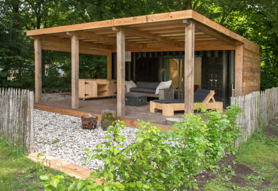 Espacio exterior en la tiny house ‘Sea container’ con terraza de madera, asientos y vallado natural.