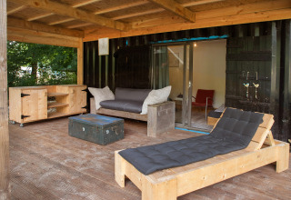 Terraza cubierta con muebles de madera y tumbona de una tiny house hecha de contenedor marítimo en Países Bajos.