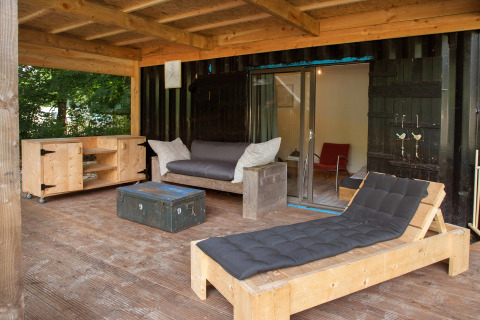 Covered wooden patio with lounge chair and sofa at a sea container tiny house in the Netherlands.