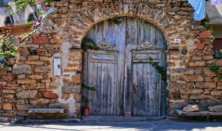 Antigua puerta de madera y arco de piedra con flores cerca de Cannigione, Cerdeña, Italia.