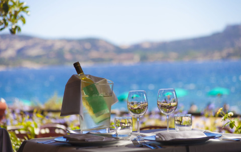 Mesa al aire libre con vino y copas frente al mar en Centro Vacanze Isuledda, Cerdeña, Italia.