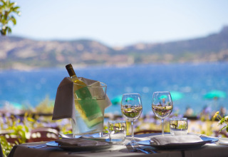 Udendørs spisebord med vin, glas og udsigt over havet på Centro Vacanze Isuledda i Sardinien, Italien.