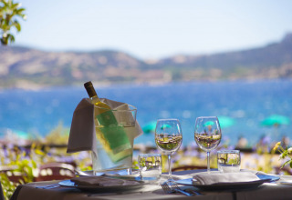 Mesa al aire libre con vino y copas frente al mar en Centro Vacanze Isuledda, Cerdeña, Italia.