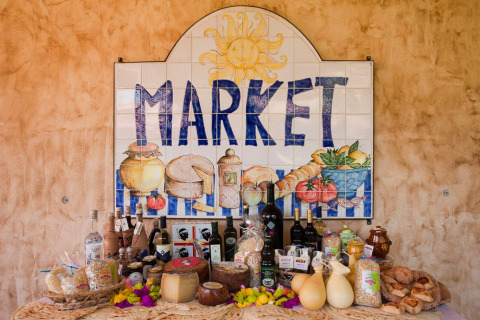 Cartel de mercado y mesa con productos sardos como quesos, vinos y pan en Centro Vacanze Isuledda.