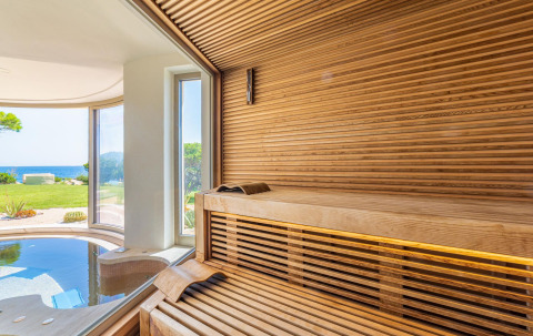 Sauna moderna in legno con vista panoramica su giardino e mare al Centro Vacanze Isuledda, Sardegna.