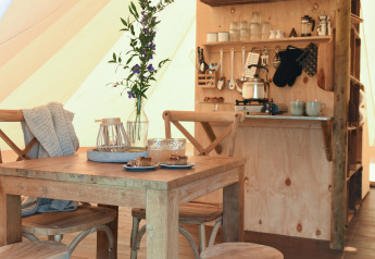 Interieur van een safari tent bij Smûk Recreatie, Nederland, met houten tafel, stoelen en keukentje.