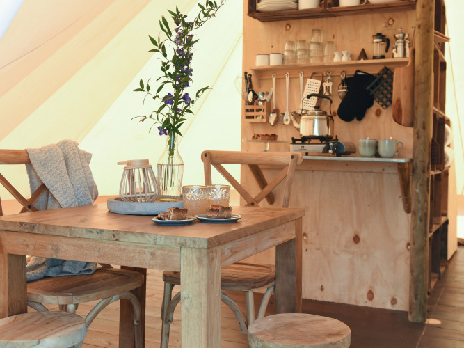 Innenaufnahme eines Safari-Zeltes mit Holztisch, Stühlen, Küche und Blumen bei Smûk Recreatie.