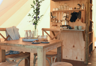 Indretning af en safari telt med træbord, stole, køkkenhjørne og blomsterdekoration på Smûk Recreatie.