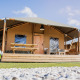 Glamping Lodge telt med træterrasse, picnicbord og moderne udendørs siddepladser under blå himmel.
