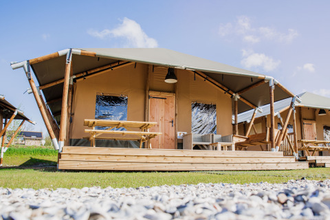 Glamping Lodge telt med træterrasse, picnicbord og moderne udendørs siddepladser under blå himmel.
