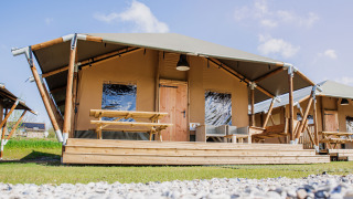 Tenda Glamping Lodge con terrazza in legno, tavolo da picnic e sedute esterne moderne sotto cielo azzurro.