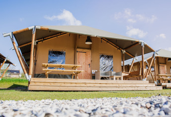 Tienda Glamping Lodge con terraza de madera, mesa de picnic y asientos modernos al aire libre soleado.