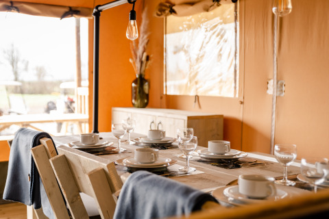 Dining table set for six inside the Glamping Lodge at Camping Waddenzee, Netherlands, with cozy decor.