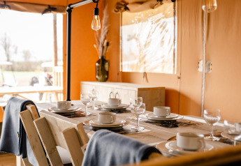 Mesa de comedor preparada para seis en la Glamping Lodge de Camping Waddenzee, Países Bajos, ambiente acogedor.