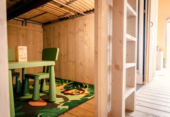 Photo intérieure d'un coin enfants avec table, chaises vertes et tapis lion à la Glamping Lodge, Camping Waddenzee.