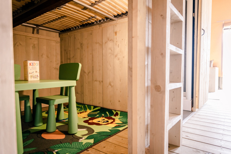 Foto interior de zona infantil con mesa verde, sillas y alfombra de león en Glamping Lodge, Camping Waddenzee.