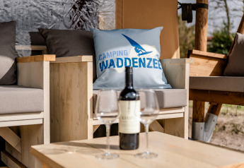 Gemütlicher Sitzbereich mit Kissen und Wein bei der Glamping Lodge am Camping Waddenzee, Niederlande.