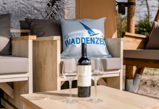 Zona de estar al aire libre con vino en la Glamping Lodge de Camping Waddenzee, Países Bajos, cojín con logo.