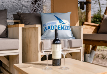 Cozy outdoor seating and wine at the Glamping Lodge, Camping Waddenzee, Netherlands, with logo pillow.