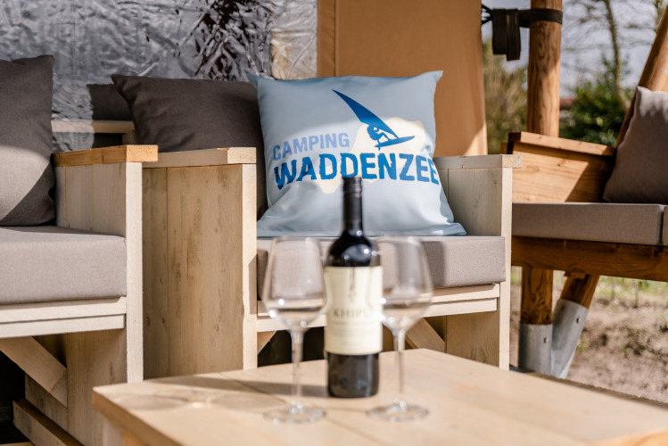 Zona de estar al aire libre con vino en la Glamping Lodge de Camping Waddenzee, Países Bajos, cojín con logo.