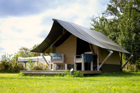 Afbeelding van een Tiny Tent lodge met terras en stoelen op een grasveld onder een lichtbewolkte lucht.