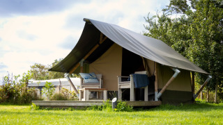 Photo d'un lodge Tiny Tent avec terrasse et chaises sur pelouse verte sous un ciel partiellement nuageux.