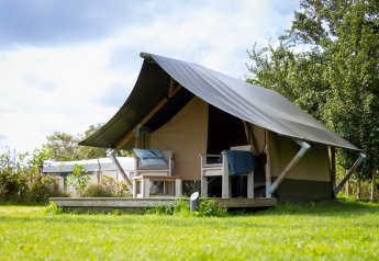 Image of a Tiny Tent lodge with a porch and chairs on a grassy lawn under a partly cloudy sky.