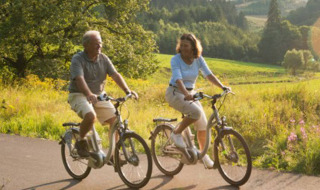 Dos adultos montan en bicicleta juntos por un sendero cerca de Deidenberg, Lieja, Bélgica, en un día soleado.