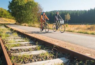 Twee fietsers fietsen naast oude spoorrails bij Camping Oos Heem in de provincie Luik, België.