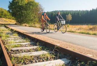 Two cyclists ride on a paved trail beside old railway tracks at Camping Oos Heem in Liège, Belgium.