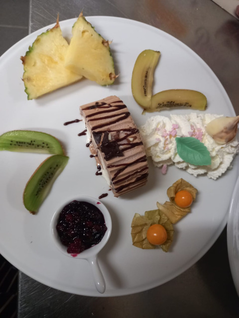 Un plato de postre bellamente decorado con frutas, nata montada, postre de chocolate y compota de frutos rojos.