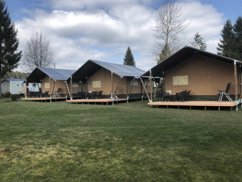 Three large glamping tents with decks on a grassy lawn at Camping Oos Heem holiday park in Liège, Belgium.
