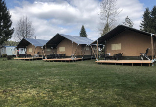Three large glamping tents with decks on a grassy lawn at Camping Oos Heem holiday park in Liège, Belgium.