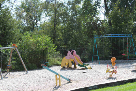 Playground with slide, swings, and seesaw surrounded by trees at Camping Oos Heem in Liège, Belgium.