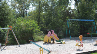 Parque infantil con tobogán, columpios y balancines rodeado de árboles en Camping Oos Heem, Lieja, Bélgica.