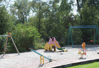Parque infantil con tobogán, columpios y balancines rodeado de árboles en Camping Oos Heem, Lieja, Bélgica.