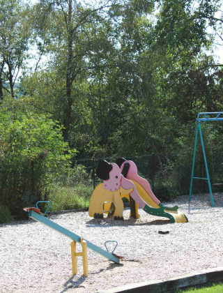 Parque infantil con tobogán, columpios y balancines rodeado de árboles en Camping Oos Heem, Lieja, Bélgica.