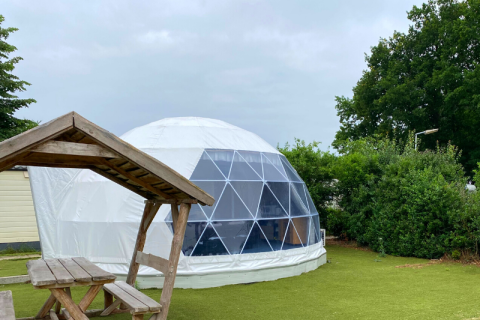 Cúpula geodésica en Costa Kabrita, Países Bajos, con mesa de picnic de madera en entorno verde.