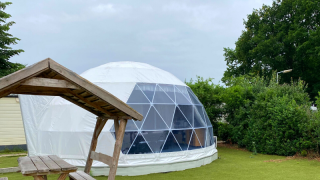 Geodetische dome-lodge bij Costa Kabrita in Nederland met houten picknicktafel en grasveld.