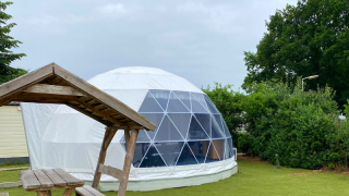 Cúpula geodésica en Costa Kabrita, Países Bajos, con mesa de picnic de madera en entorno verde.