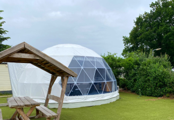 Cúpula geodésica en Costa Kabrita, Países Bajos, con mesa de picnic de madera en entorno verde.