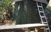Boomhut Treelodge bij Costa Kabrita in Nederland, met ladder en camouflagenet in een bosrijke omgeving.