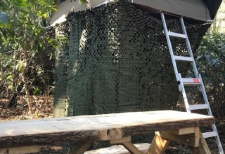 Boomhut Treelodge bij Costa Kabrita in Nederland, met ladder en camouflagenet in een bosrijke omgeving.