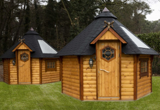 Twee achthoekige houten huisjes met zwarte daken op het gras bij Finse Kota, Costa Kabrita in Nederland.